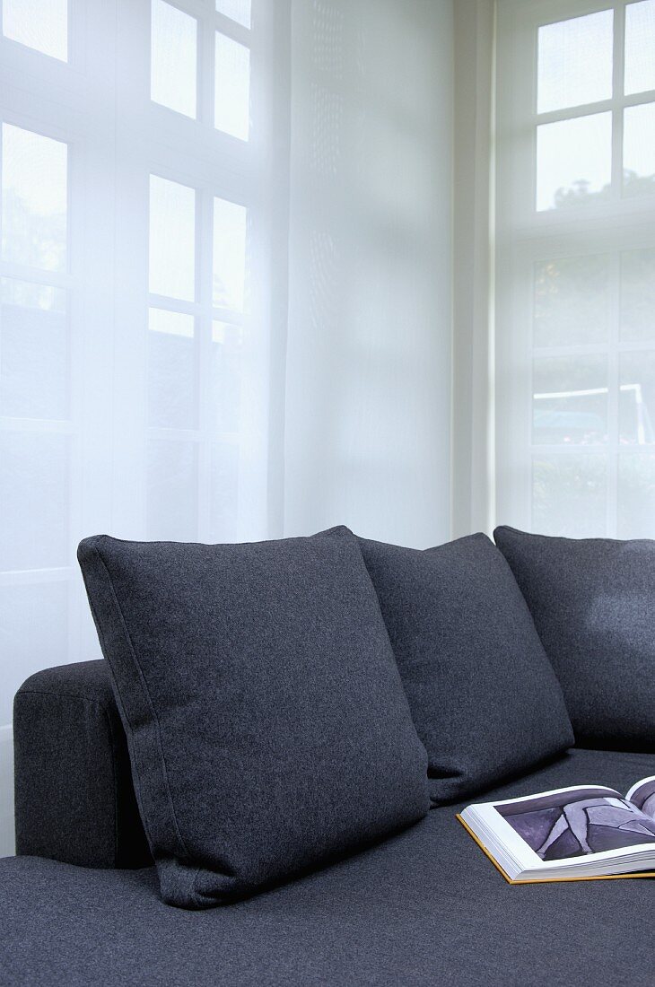 Graue Sofakissen passend zum Sofa vor transparentem Vorhang in Wohnzimmerecke