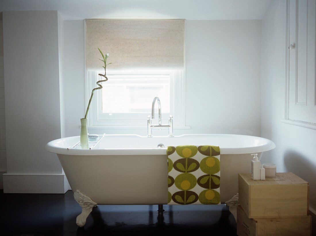 Free-standing, vintage bathtub with retro-patterned towel draped over rim