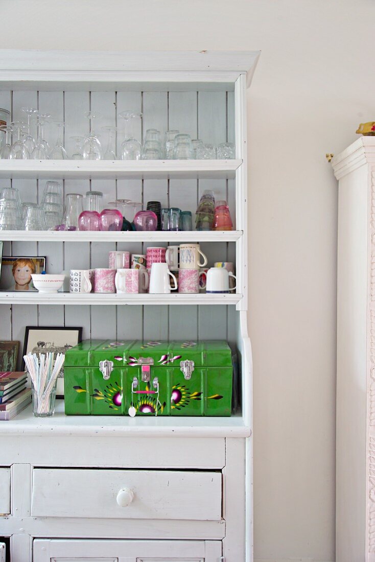 Glasses, cups and painted wooden case on white-painted kitchen dresser