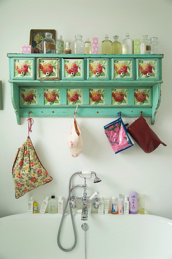 Painted, wall-mounted rack with flower motif and collection of antique bottles above vintage-style bathtub tap fittings