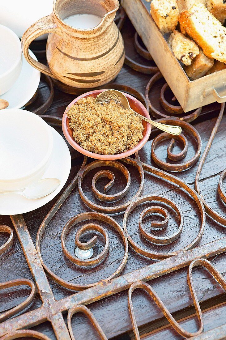 Ausschnitt einer rustikalen Kaffeetafel mit verschnörkeltem Metallgitter auf Gartentisch