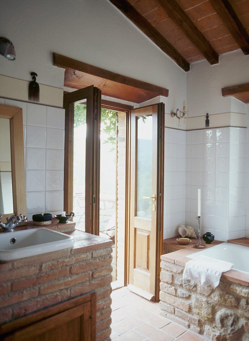 Waschtisch und Badewanne mit Ziegelsteinmauer im modernisierten Bad und offenstehender Terrassentür