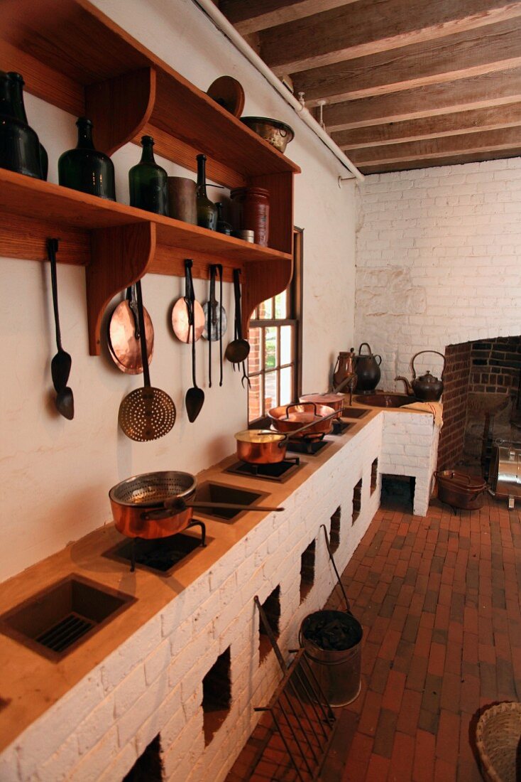 Rustikale Küche mit mehreren Feuerstellen in gemauerter Küchenzeile und Kochgeschirr aus Kupfer