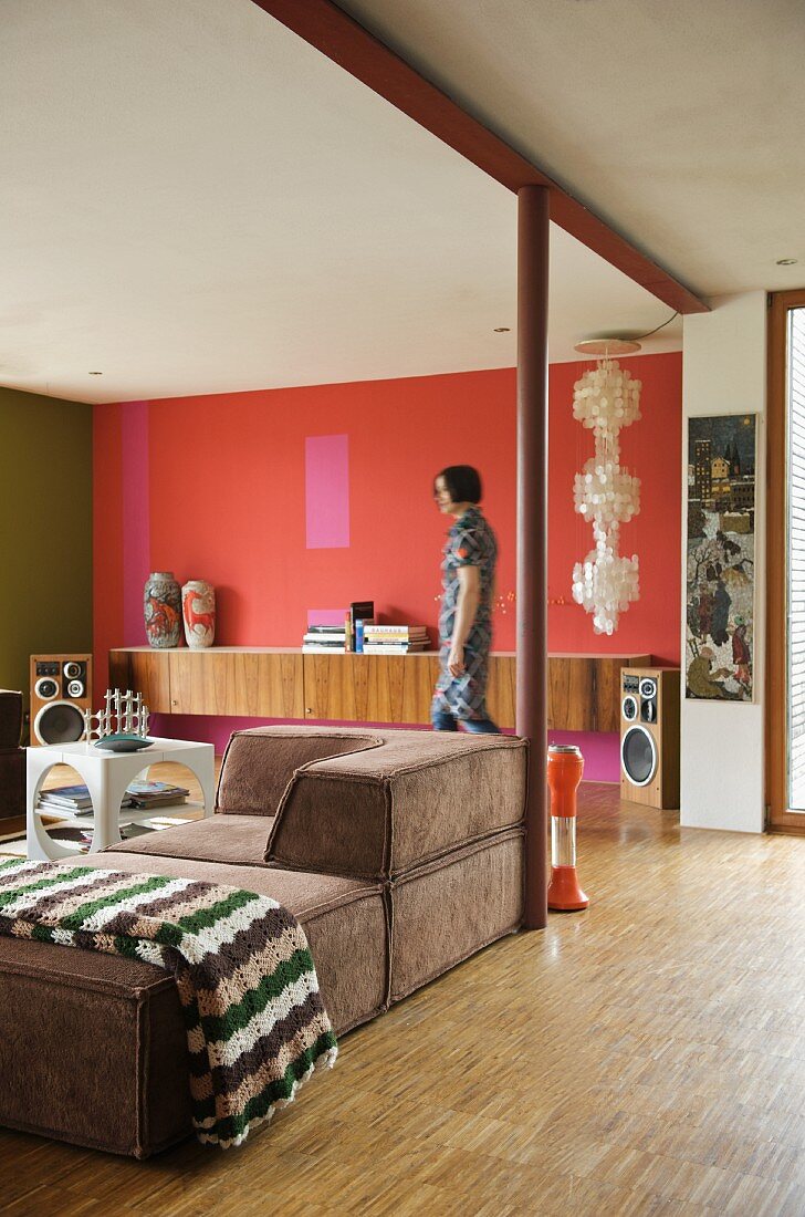 Braunes Polstersofa im Retro Wohnraum mit rot getönter Wand