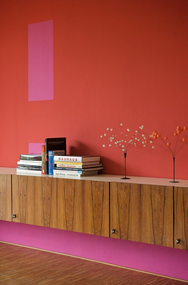 Sideboard aus Holz vor Wand mit verschiedenen Rottönen
