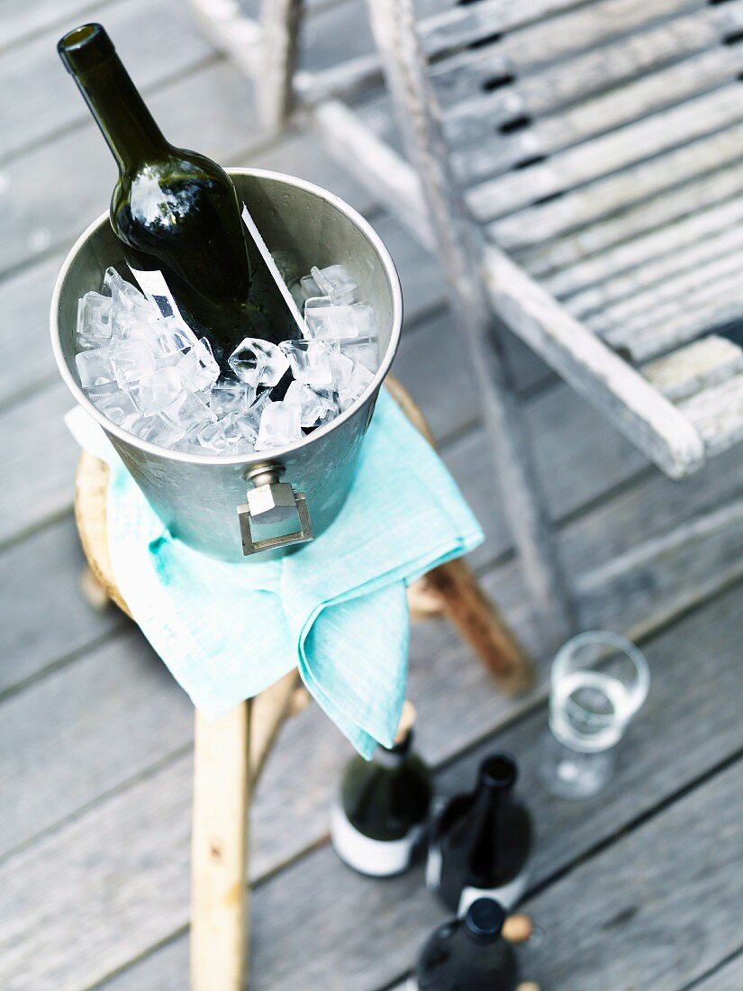 Bottle of red wine in an ice bucket on a stool on a veranda