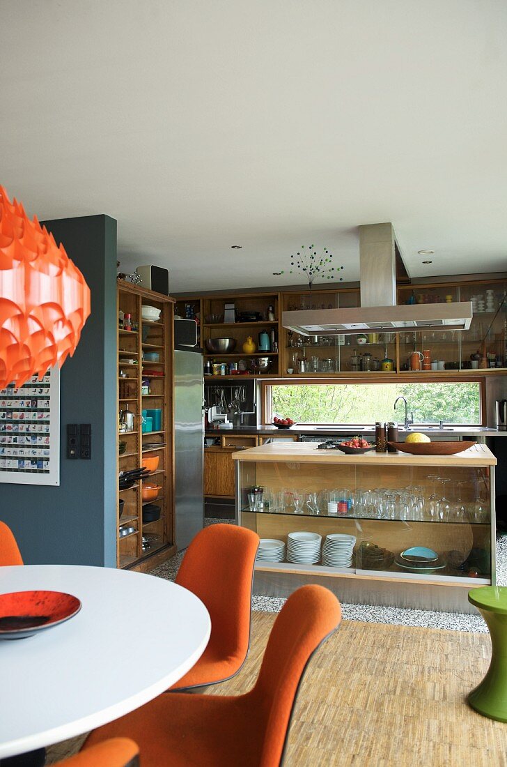 Essplatz mit orangem Polster auf Stühlen vor offener Küche mit Küchenblock