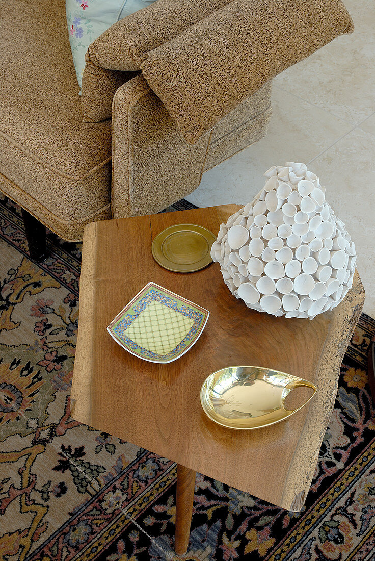 Verschiedene Schalen auf schlichtem Beistelltisch aus Holz im Fiftiesstil und teilweise sichtbares Sofa mit Armlehne