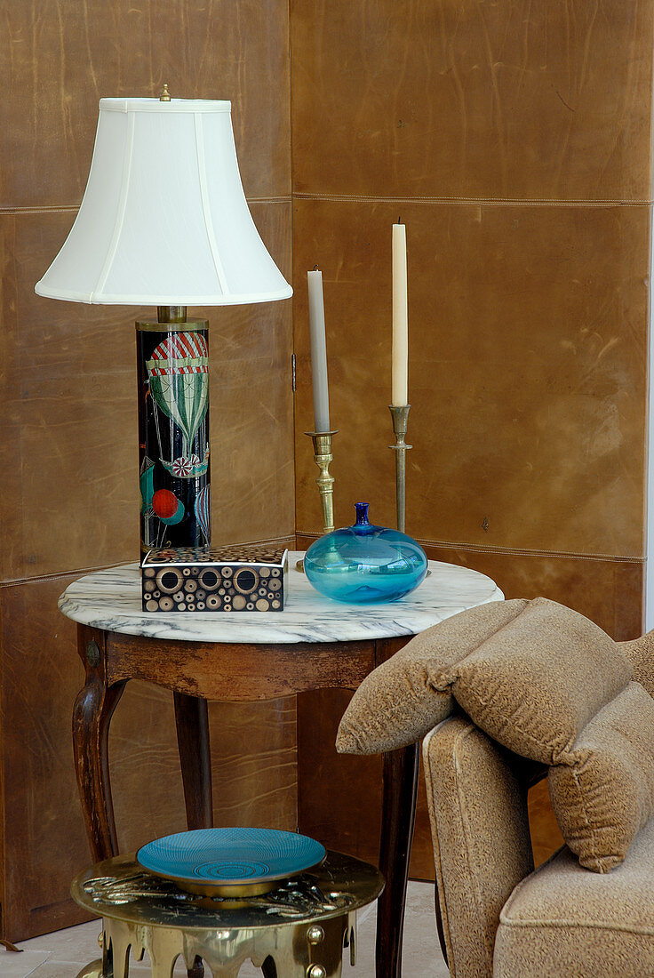 Tischlampe mit weißem Schirm und Kerzenständern auf traditionellem Beistelltisch in Zimmerecke vor lederbezogenen Paneelen an Wand