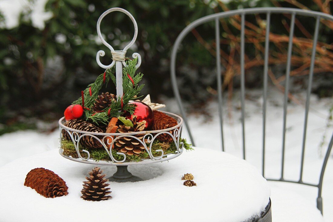 Metall-Etagere mit Naturdeko und roten Kugel auf Gartentisch im Schnee