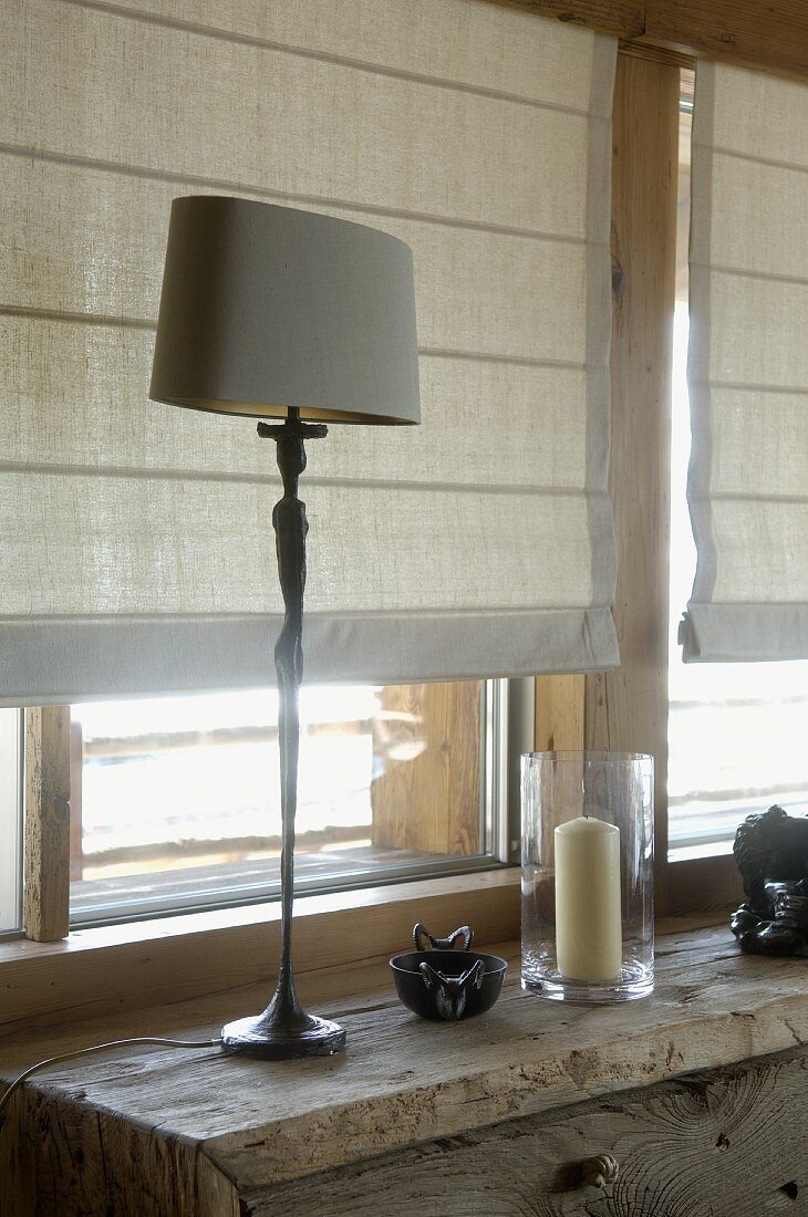 Tischlampe auf rustikalem Schränkchen vor Fenster mit halbgeschlossenem Rollo