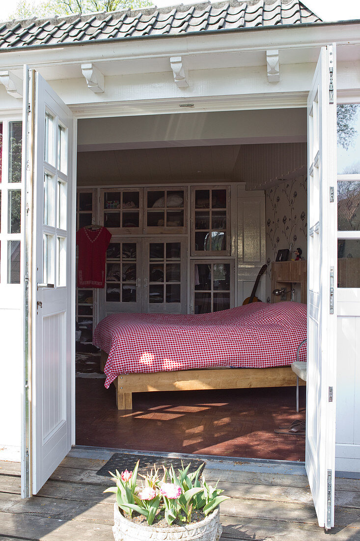 Weiß lackiertes Holz in historischem Landhaus - Blick von Terrasse durch zweiflügelige Tür auf weiss-rot karierterte Bettdecke