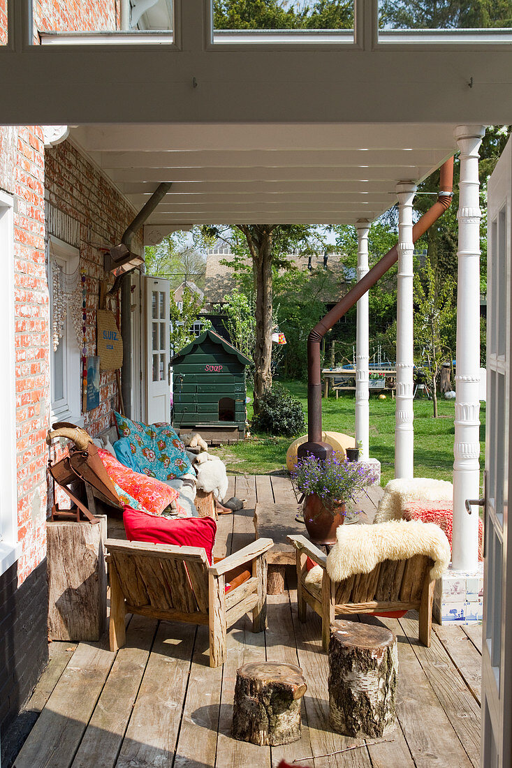 Rustic wooden chairs with colourful cushions and furs on a covered wooden terrace with antique steel chairs