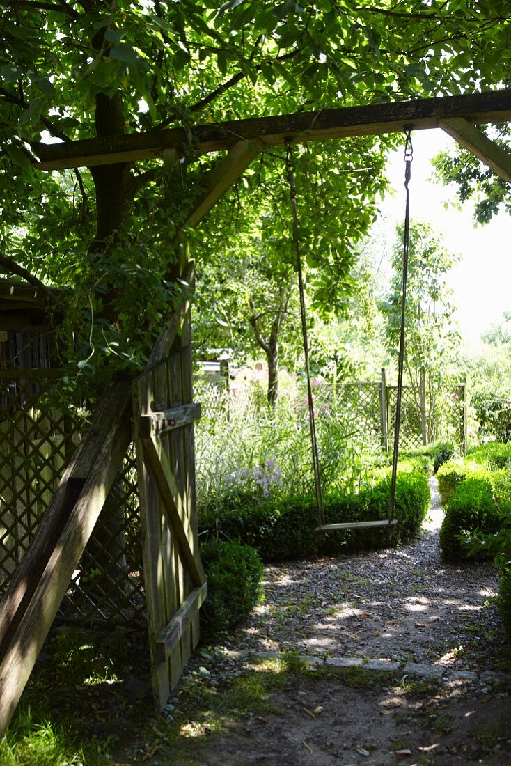 Bauerngarten mit offenem Gartentor und einer am Torbogen hängenden Kinderschaukel