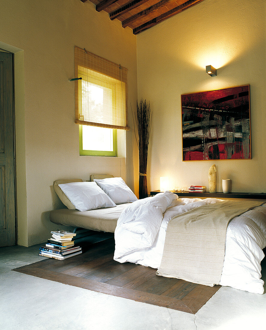 Bedroom with concrete and wood floor, modern painting on wall and warm light from sconce lamp