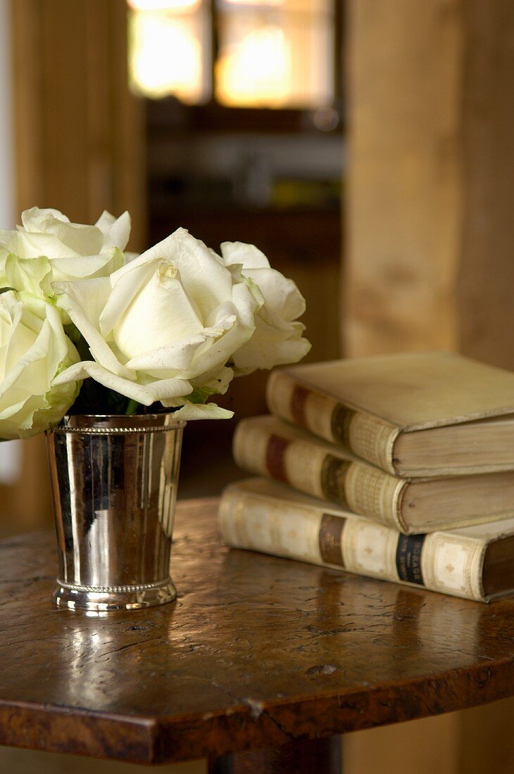 White roses in a silver cup and antique books on an old table top