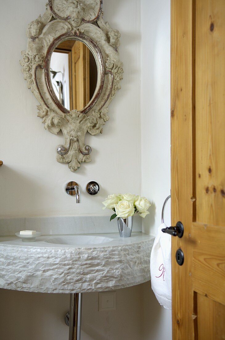 Playful, antique style mirror above a modern sink made of hewn stone