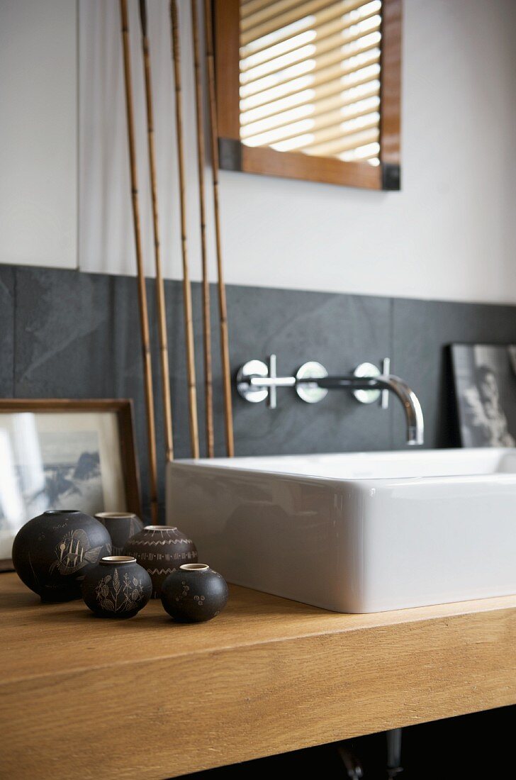 White countertop washbasin on wooden washstand decorated with small, anthracite-coloured ceramic vases