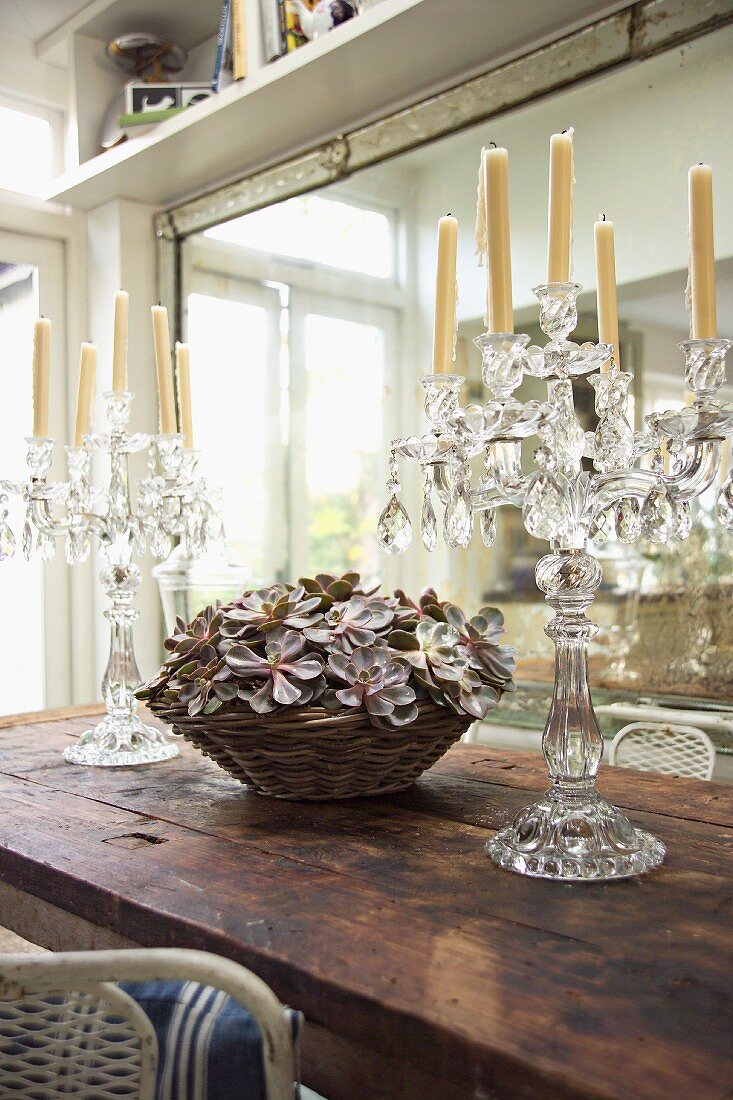 Kristall-Kerzenständer und Körbchen mit Blütendeko auf altem Holztisch