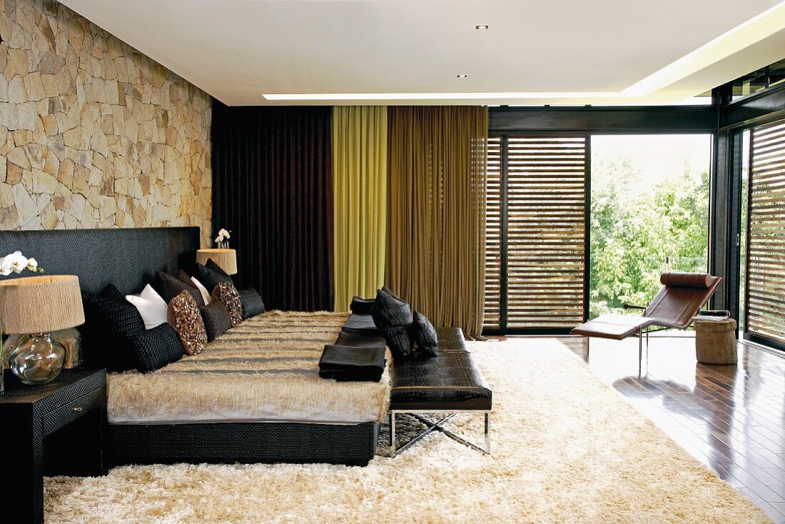 Modernes Schlafzimmer mit Fell und Leder; Liege vor großen, offenen Schiebejalousien