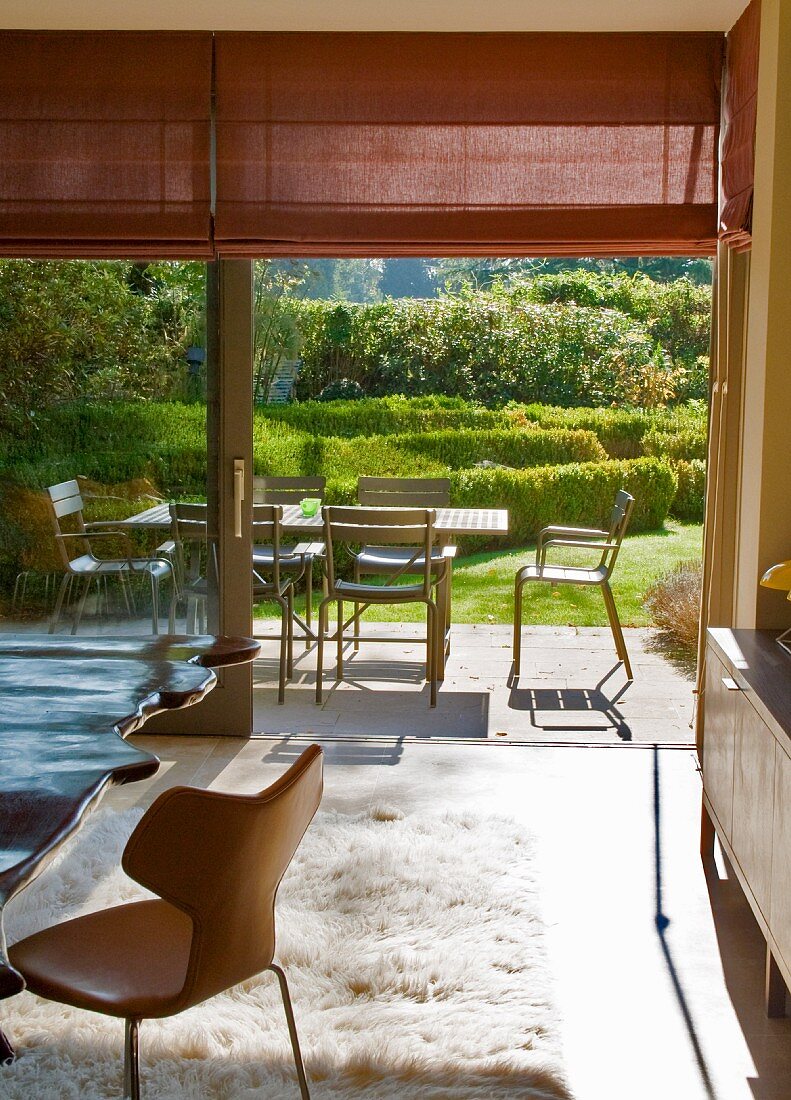 Interior with seating area on flokati rug in front of open terrace door with view of table and chairs in sunny garden
