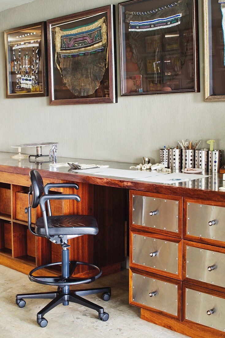 Bürostuhl vor Arbeitstisch aus Holz mit eingebautem Schubladenschrank und Edelstahlfronten