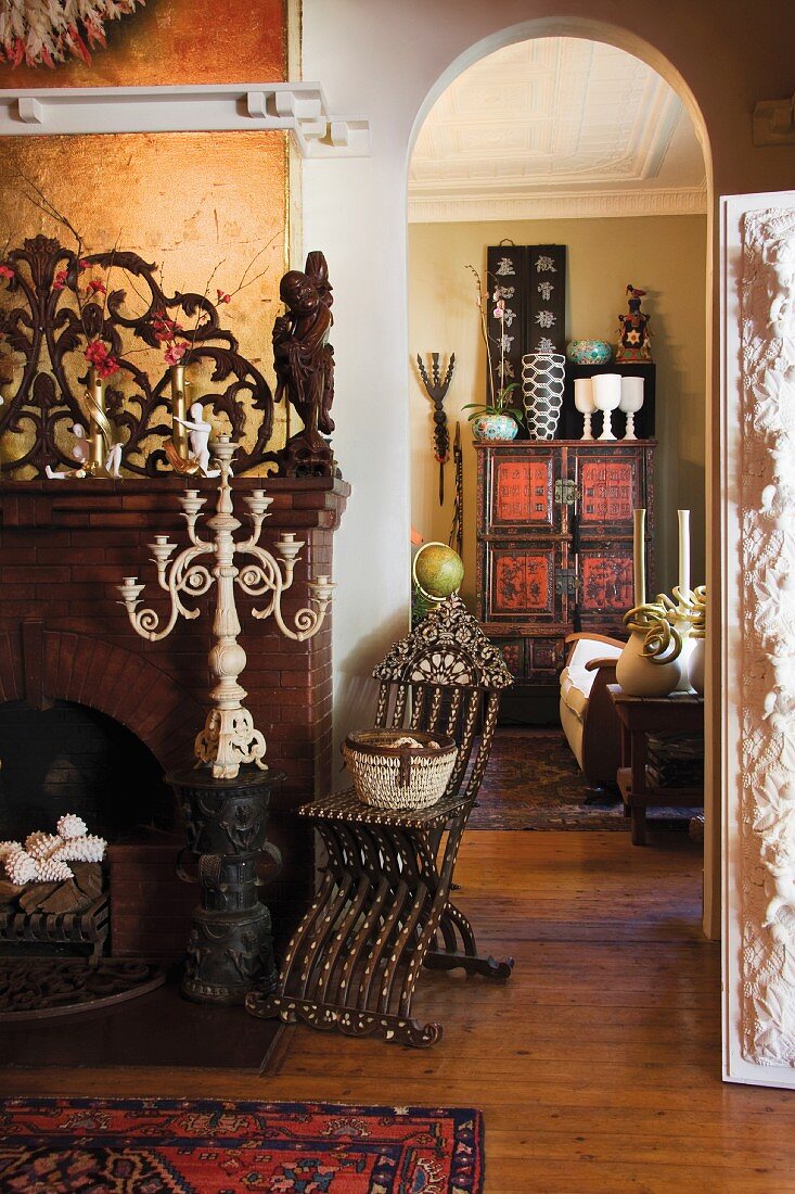 Open fireplace with a dark brick surround and a carved wooden upper section; in front, a candelabra on a carved wooden pedestal, in the background an antique, Chinese cabinet