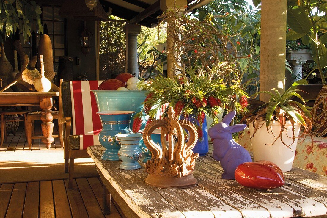Sonnige Holzterrasse mit Vintage-Tisch, Blumen und bunten Dekorationsobjekten