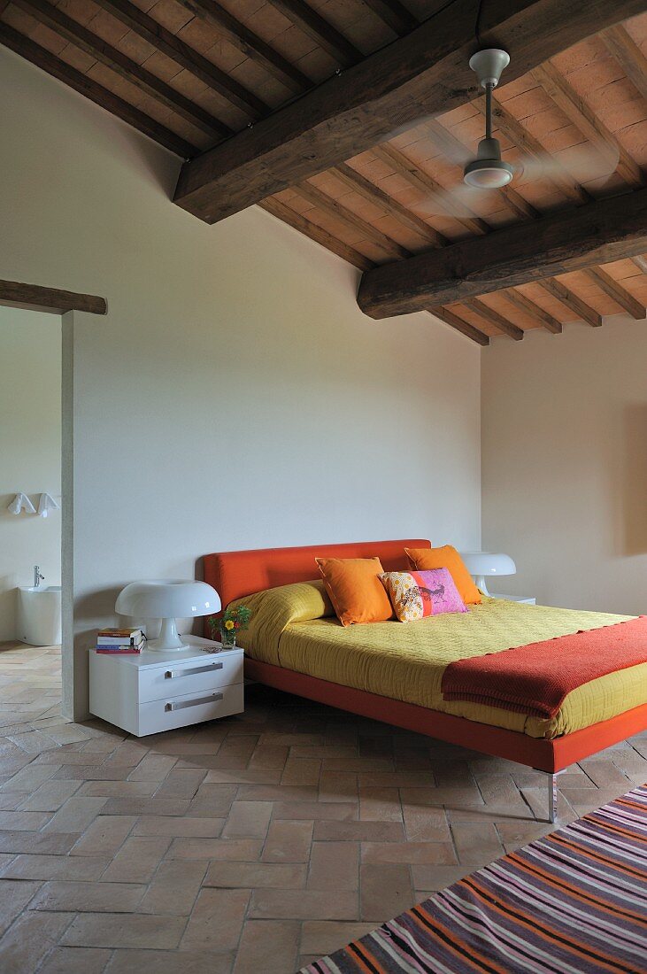 Purist bedroom with designer bed on old terracotta floor below rustic ceiling