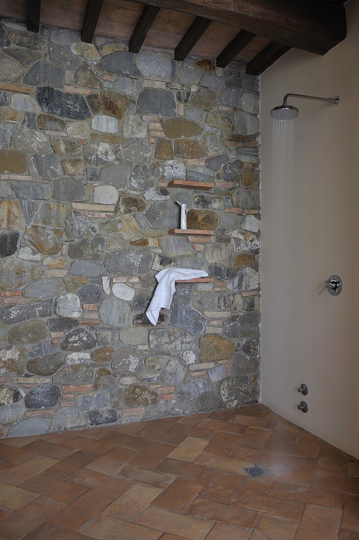 Shower head with running water in floor-level shower with stone wall