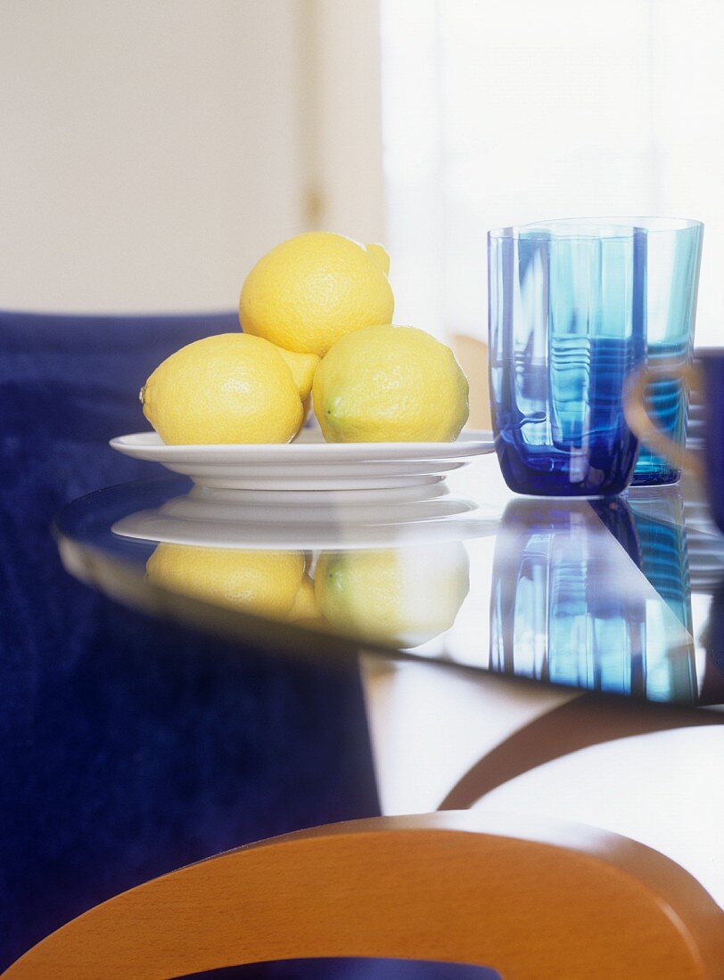 Lemons on a plate next to colored water glasses on a table