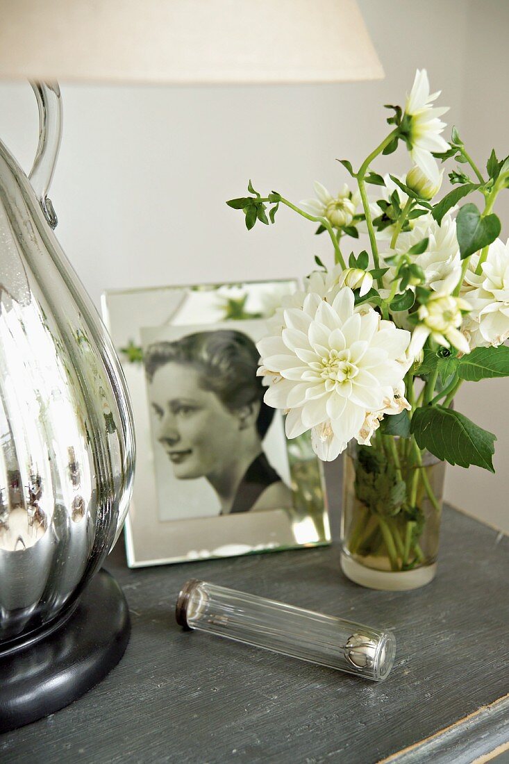 weiße Blumen in Glasvase neben gerahmter Photographie