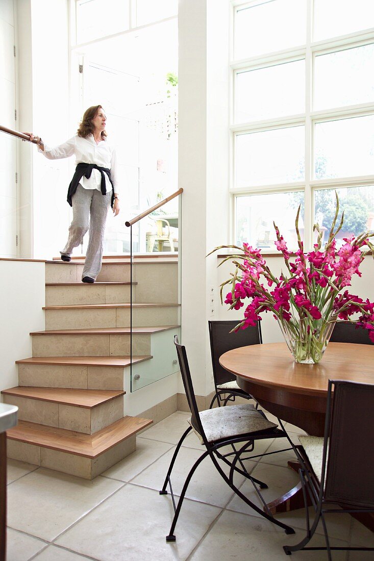Woman walking down stairs in light foyer with dining area