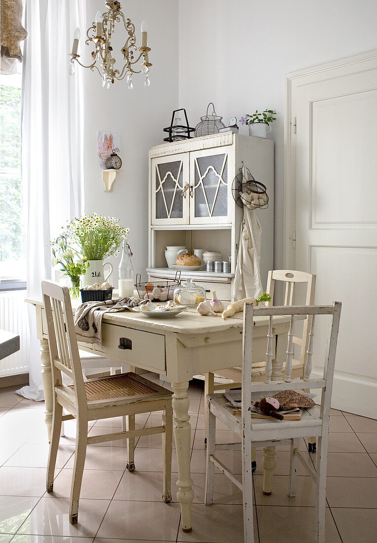 Rustic dining area with white-painted chairs around table; dresser in background