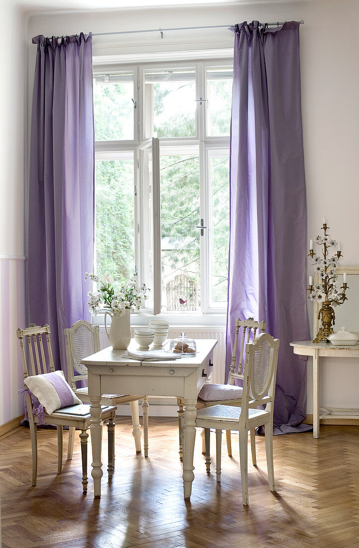 Alte französische Stühle um Holztisch im gustavianischem Stil neben Fenster mit bodenlangen, violetten Vorhängen