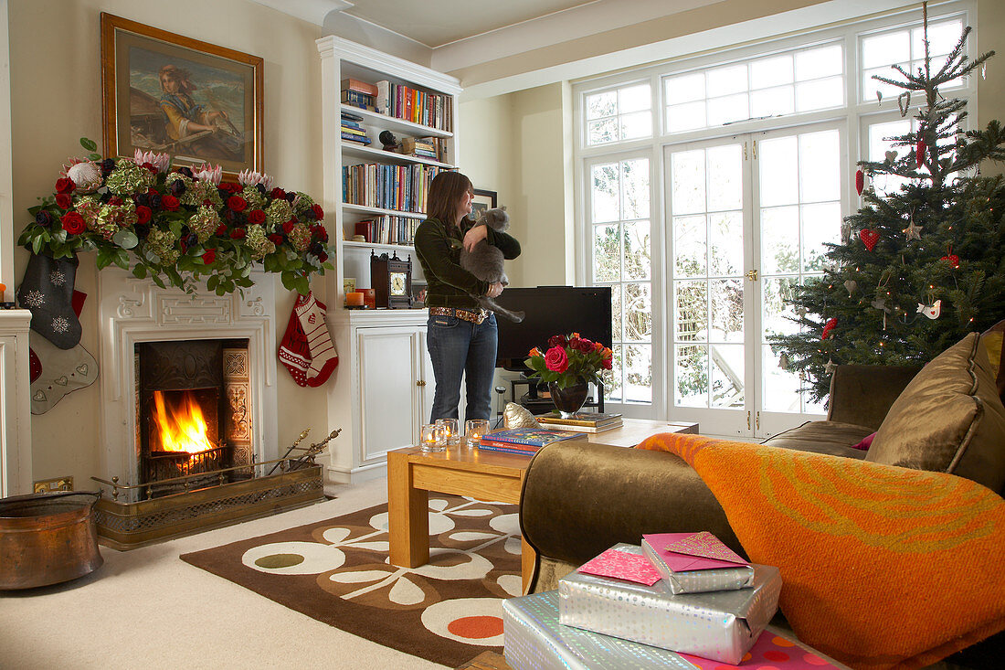 Weihnachtlich geschmücktes Wohnzimmer in englischem Landhaus; Frau mit Katze auf dem Arm im Hintergrund