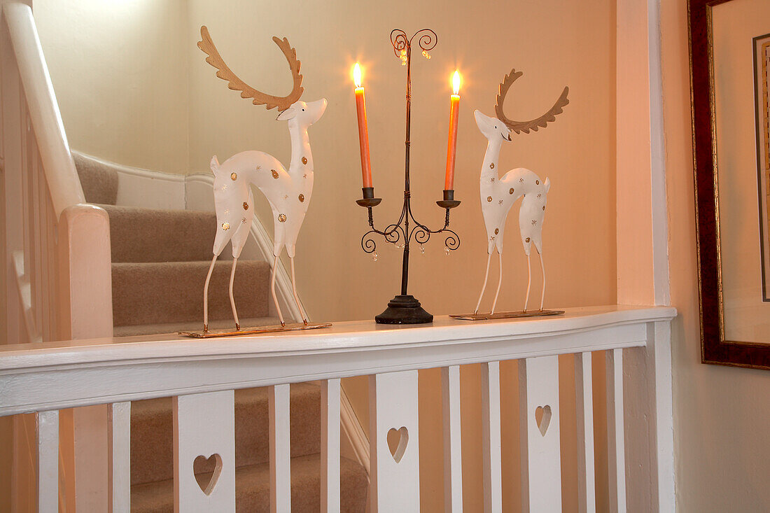 Advent arrangement of stylised stags and candelabra with lit candles on wooden landing balustrade in country house