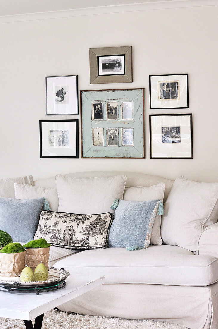 Framed black and white photographs above pale, country house sofa with scatter cushions