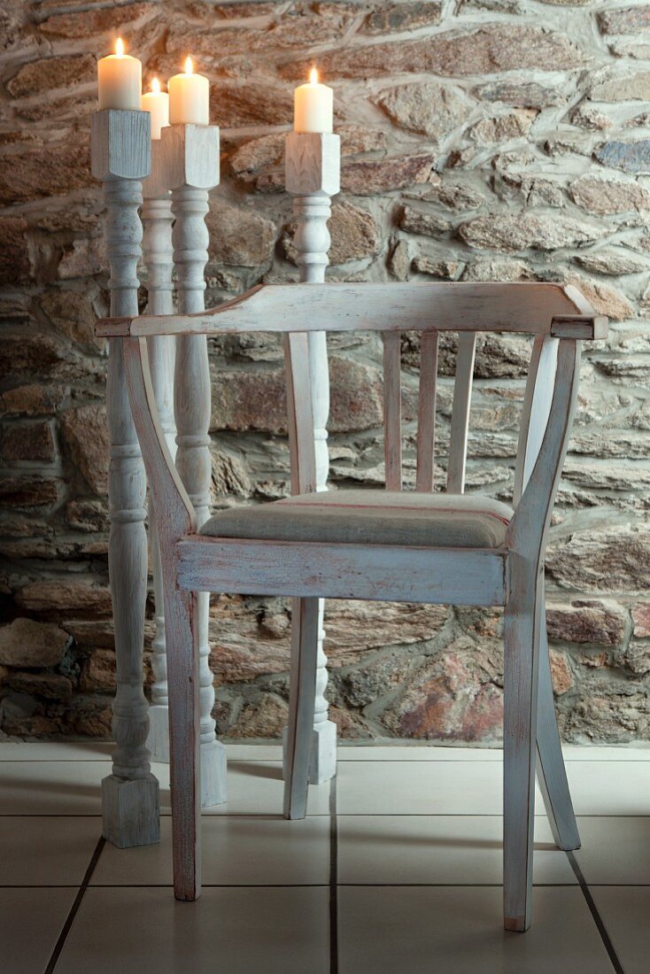 Weisser Holzstuhl und Bodenkerzenleuchter aus alten Tischbeinen vor Natursteinmauer