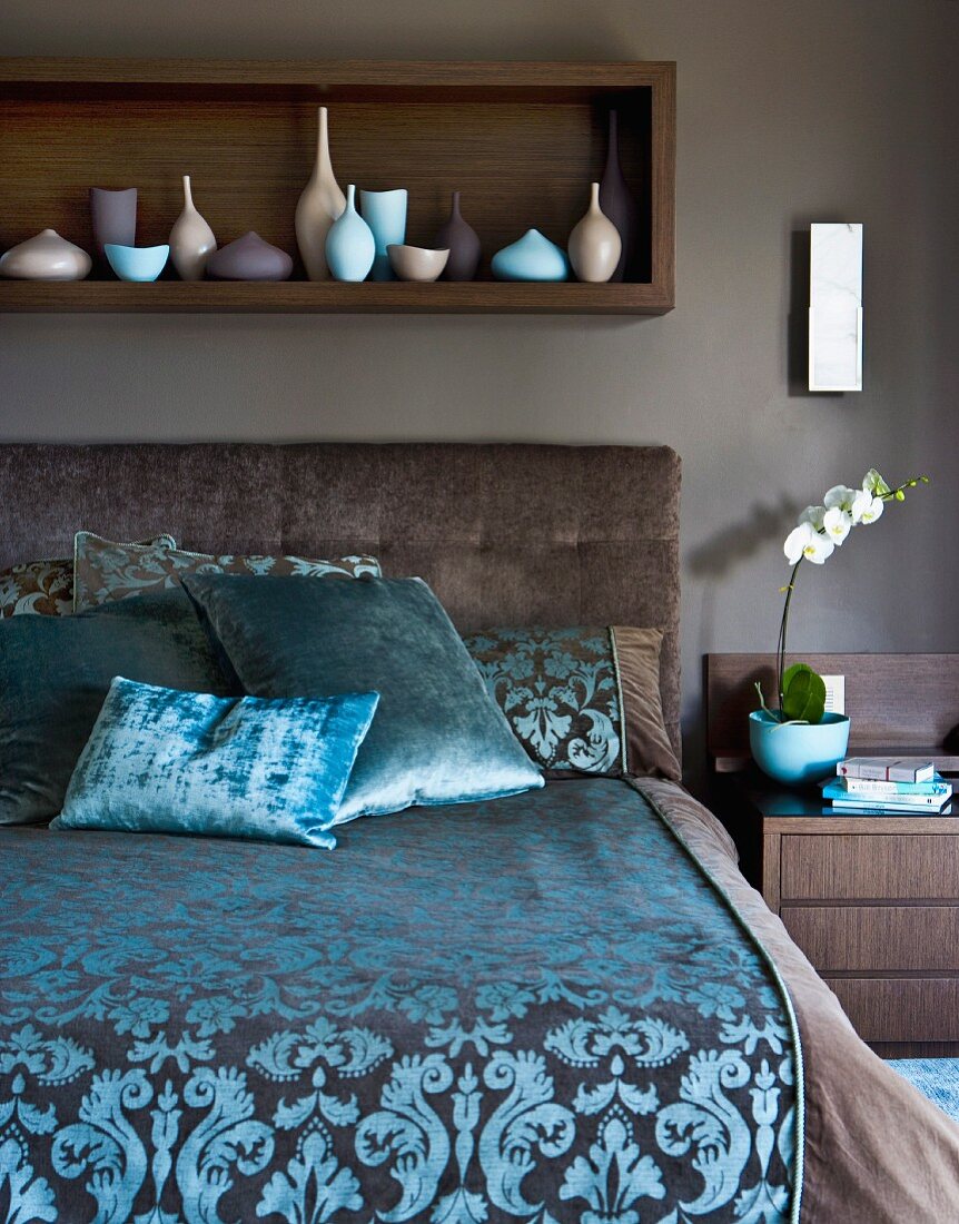Elegant bed with patterned satin cover against brown-painted wall