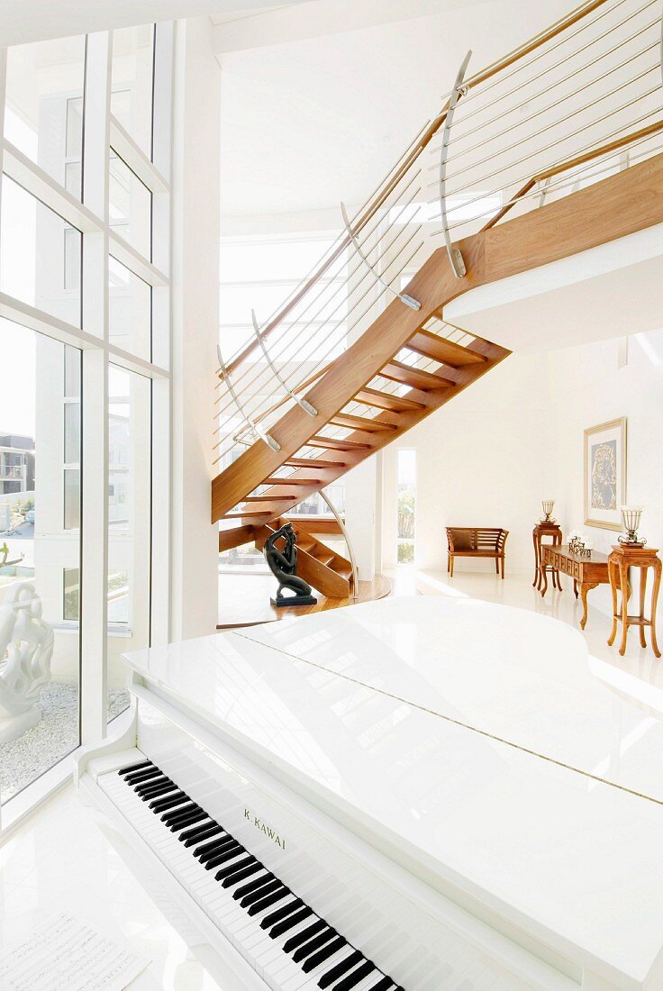 Weiß glänzender Flügel im zweigeschossigen Wohnraum mit offener Designertreppe vor raumhoher Fensterfront