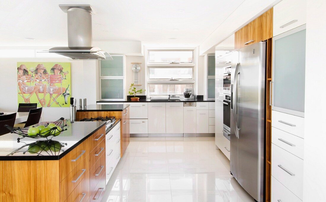 Küchenblock und übergrosser Edelstahlkühlschrank in breiter, offener Küche mit Fronten in Weiß und Holz