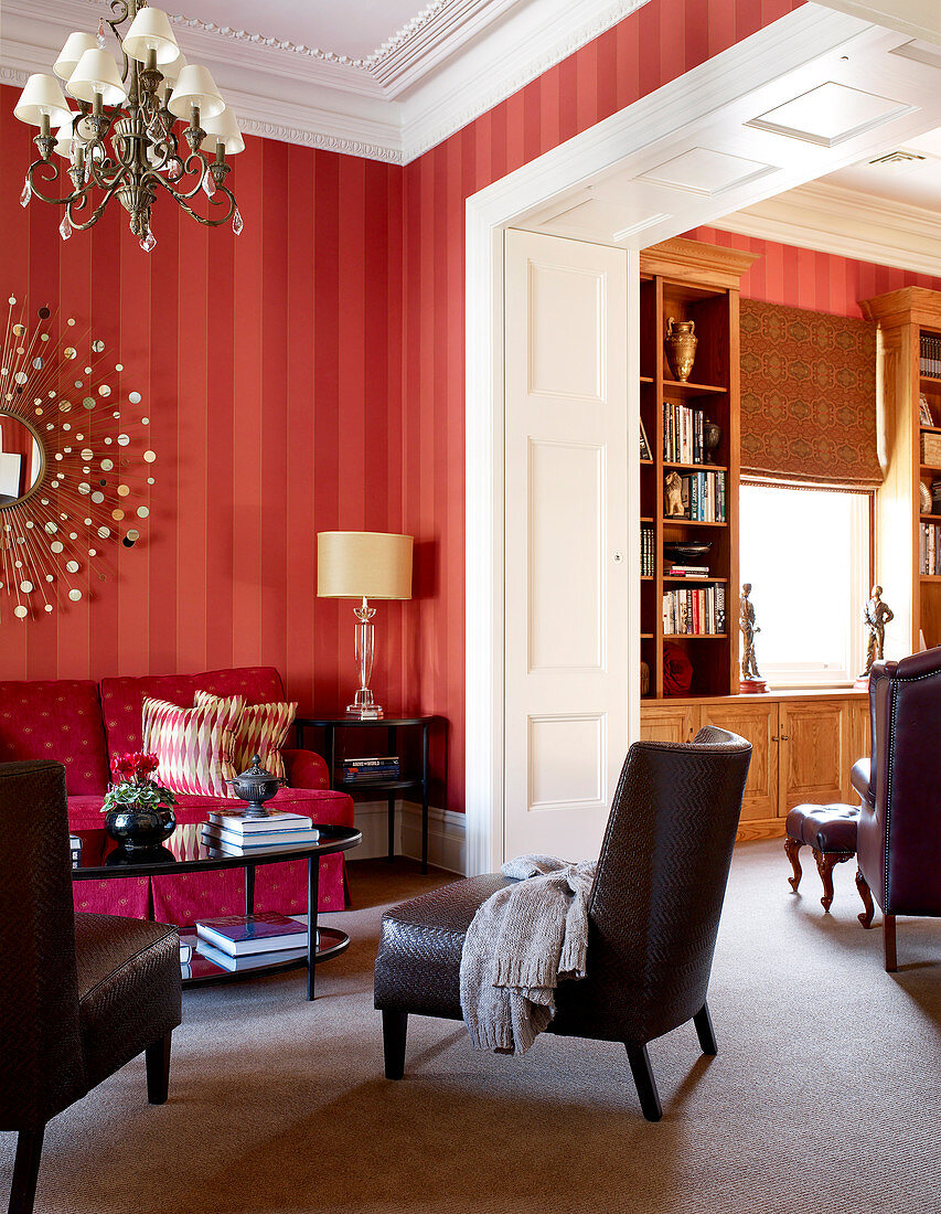 Warme Rottöne in traditionellem Wohnzimmer mit pinkfarbener Couch und anschliessender Bibliothek