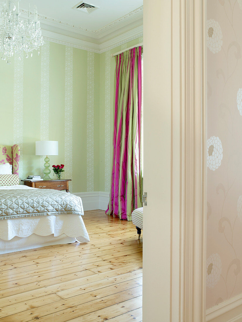 Pale green bedroom with simple wooden floor and colourful curtains with pink stripes