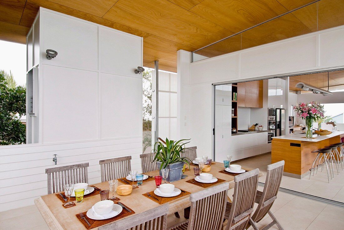 Holzklappstühle an gedecktem Esstisch und Blick durch breiten Durchgang in Küche auf Theke mit Barhockern