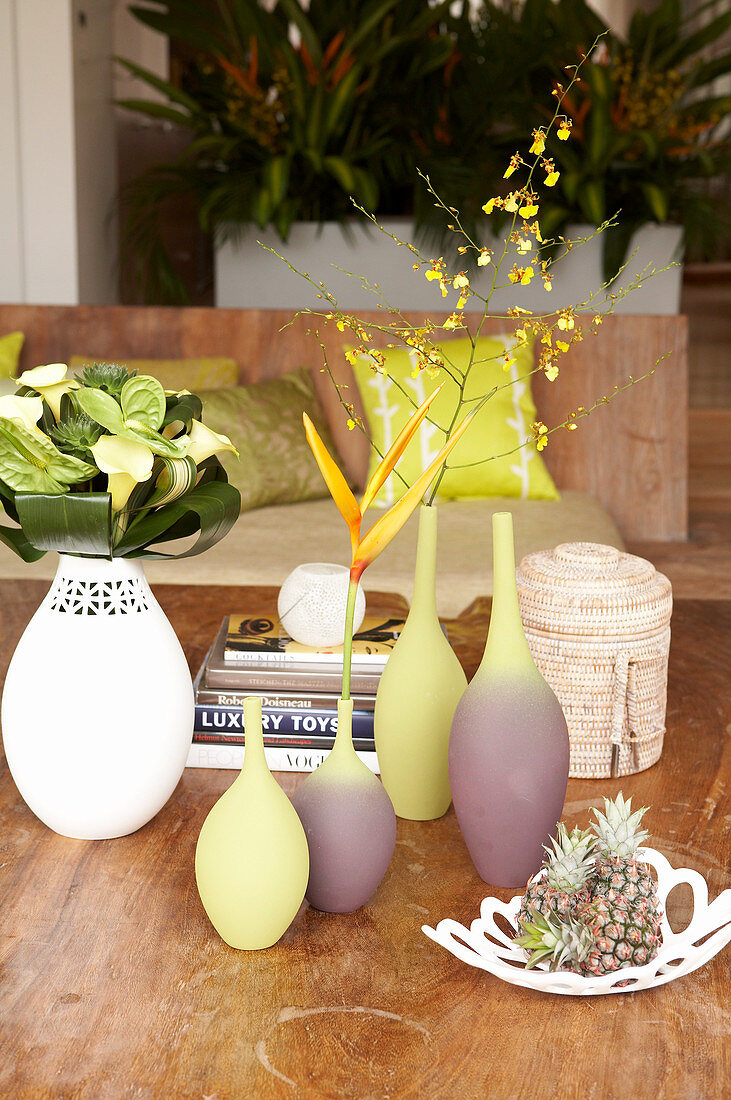 Vasengruppe mit einzelnen Blumen und Obstschale auf dem Holztisch