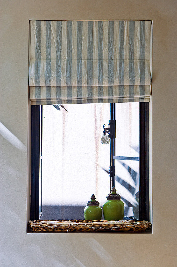 Antique, green glazed, ceramic containers and striped Roman blind at a window with outward opening windows