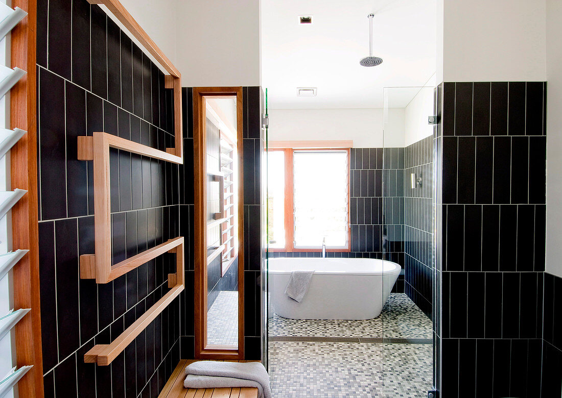 Blick von Sauna durch offene Glastür auf freistehende Badewanne in schwarz gefliestem Designerbad