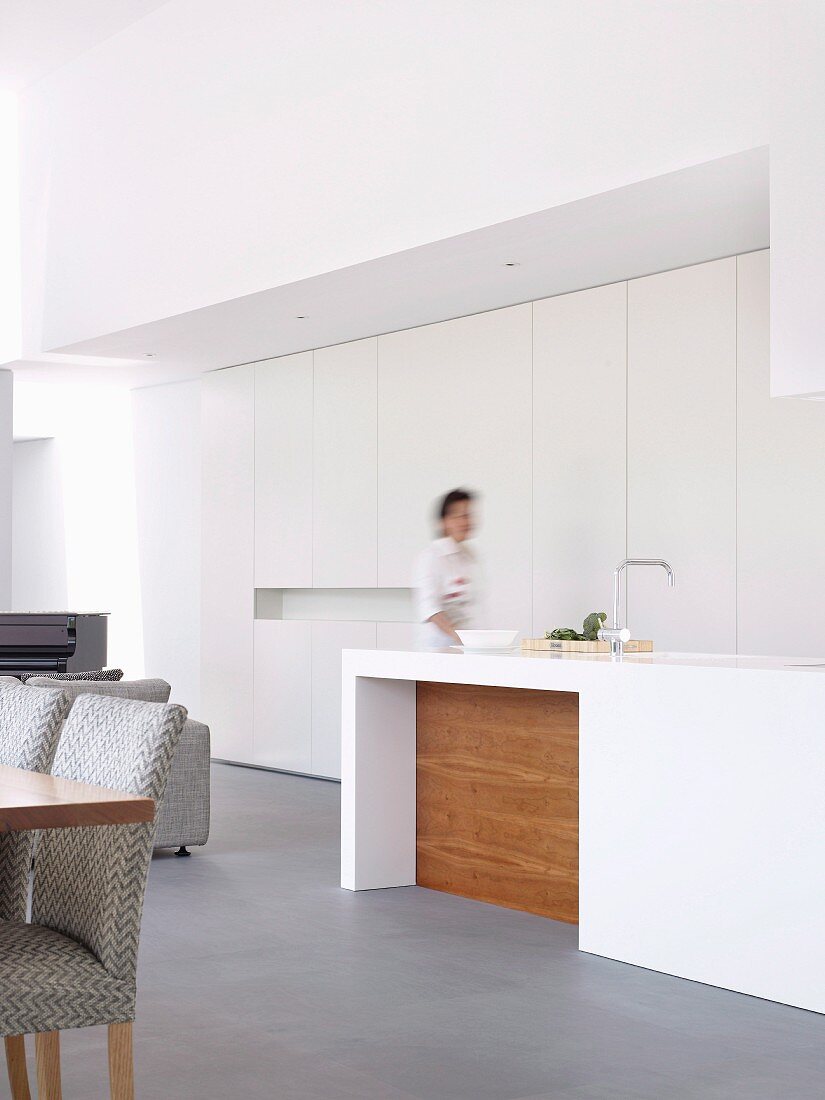 Woman at white designer kitchen counter in front of fitted cupboards in open-plan interior