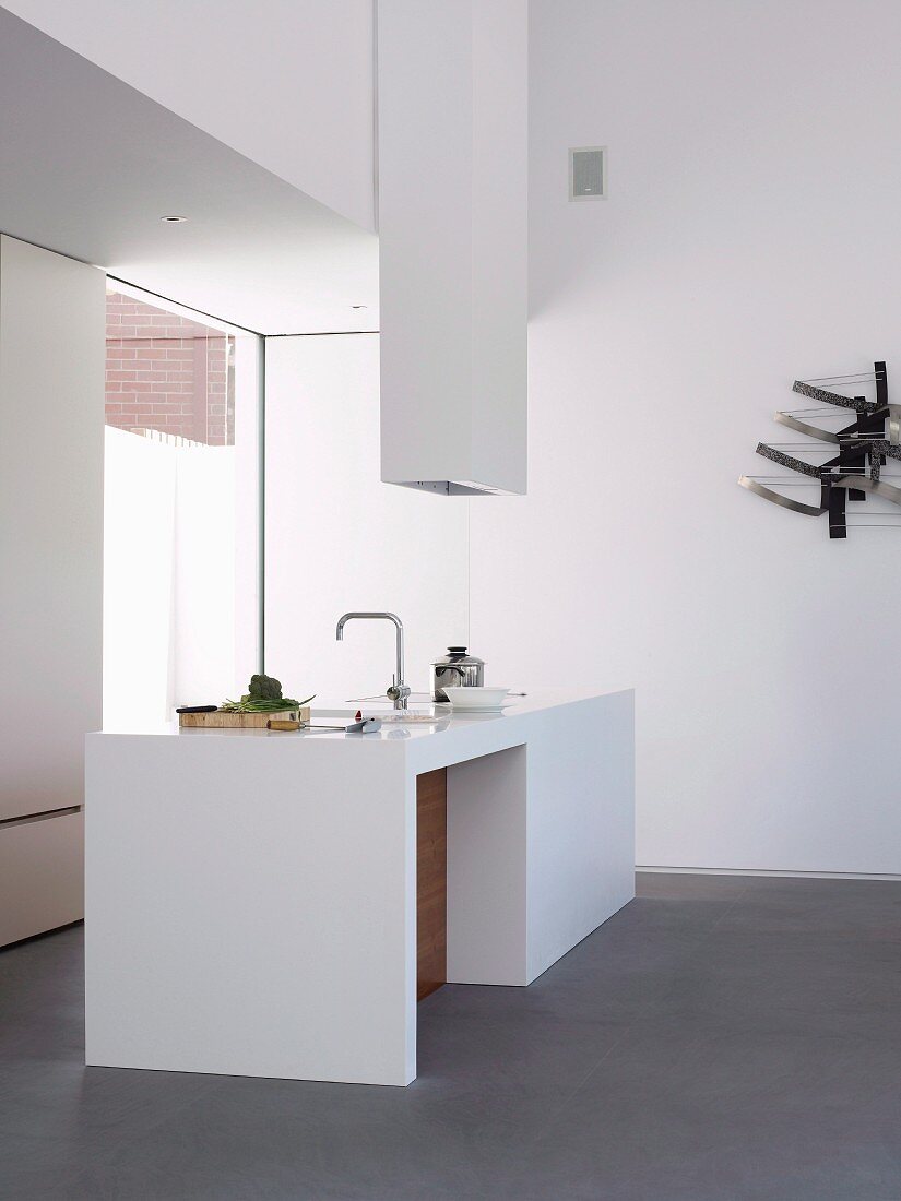 White, designer minimalist kitchen island with extractor hood in corner of room with floor-to-ceiling window